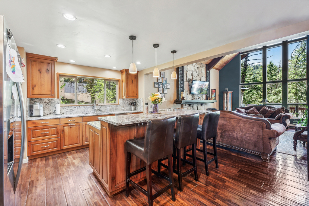 Kitchen with light stone counters, backsplash, pendant lighting, and dark wood-type flooring