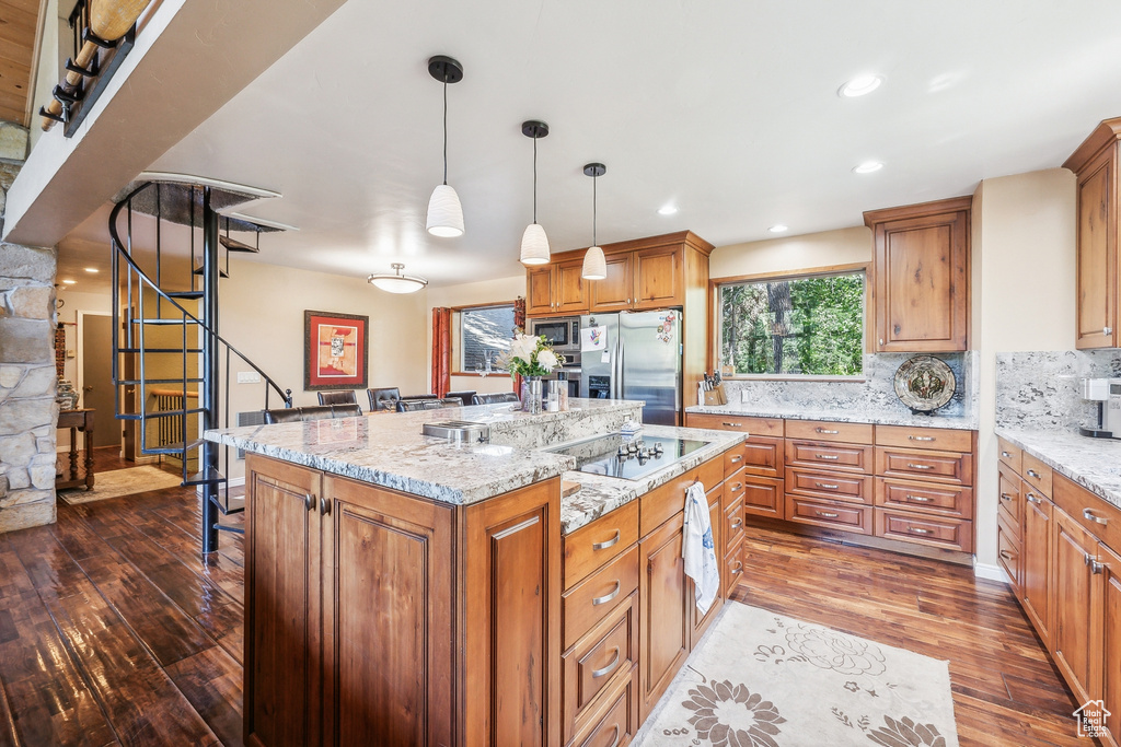 Kitchen with decorative light fixtures, a kitchen island, tasteful backsplash, hardwood / wood-style flooring, and appliances with stainless steel finishes