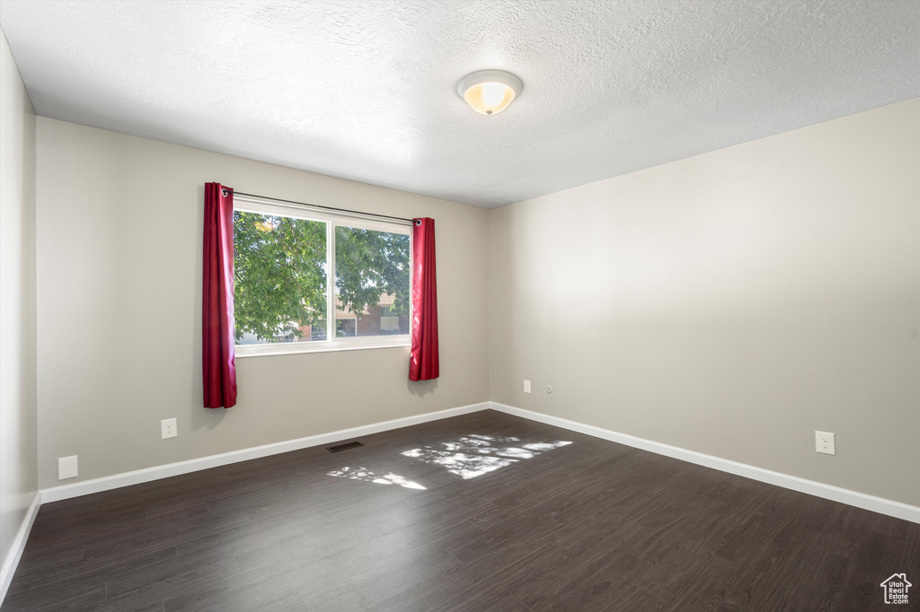 Empty room featuring dark hardwood / wood-style flooring and a textured ceiling