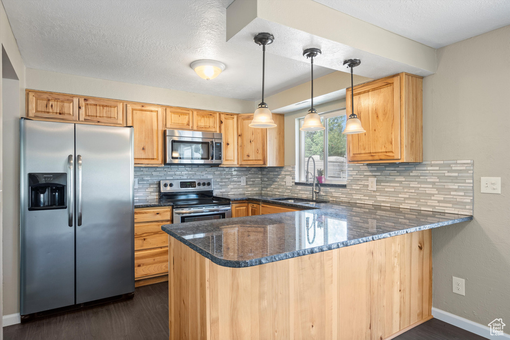 Kitchen featuring appliances with stainless steel finishes, kitchen peninsula, dark hardwood / wood-style flooring, and decorative light fixtures