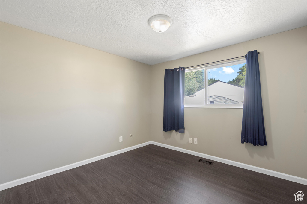 Empty room featuring dark hardwood / wood-style floors and a textured ceiling