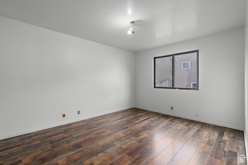 Empty room with a textured ceiling and dark wood-type flooring