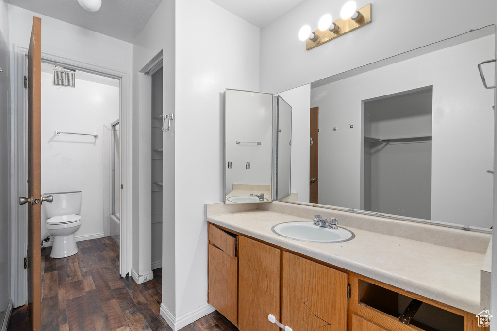 Full bathroom with toilet, vanity, combined bath / shower with glass door, and hardwood / wood-style flooring
