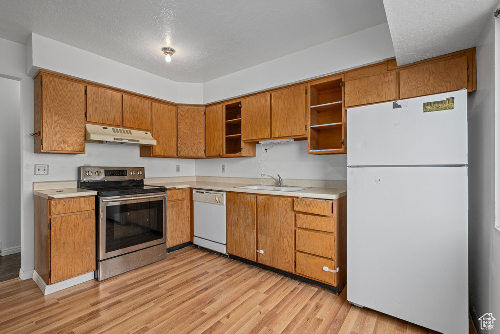 Kitchen featuring a textured ceiling, light wood-type flooring, white appliances, and sink