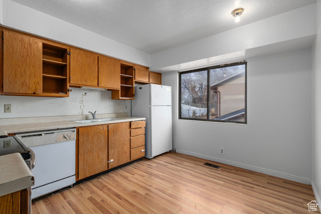 Kitchen with white appliances, light hardwood / wood-style floors, and sink