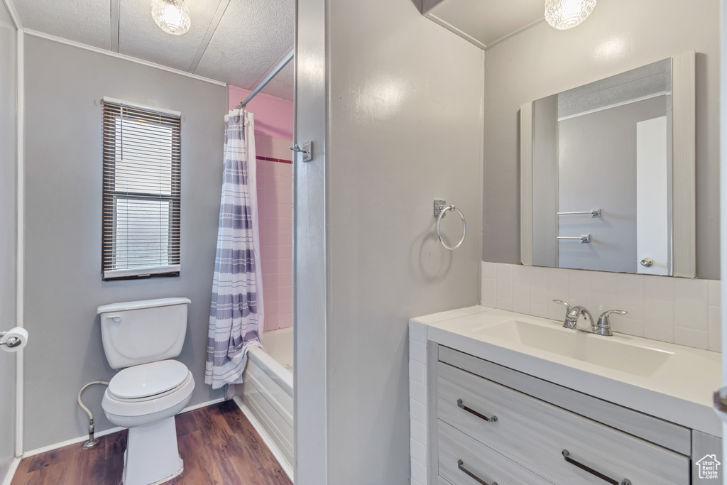 Full bathroom with backsplash, toilet, vanity, shower / bath combo with shower curtain, and wood-type flooring