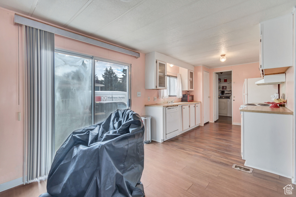 Kitchen with white cabinetry, independent washer and dryer, light wood-type flooring, and white appliances