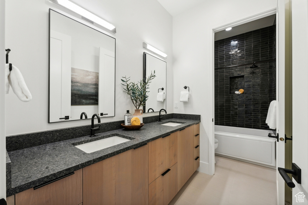 Full bathroom with tile patterned floors, double vanity, tiled shower / bath combo, and toilet