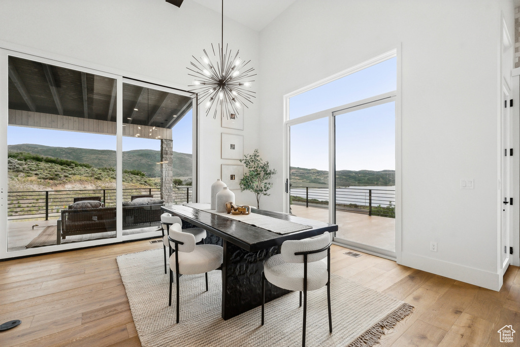 Dining space with a healthy amount of sunlight, light hardwood / wood-style floors, a towering ceiling, and a chandelier