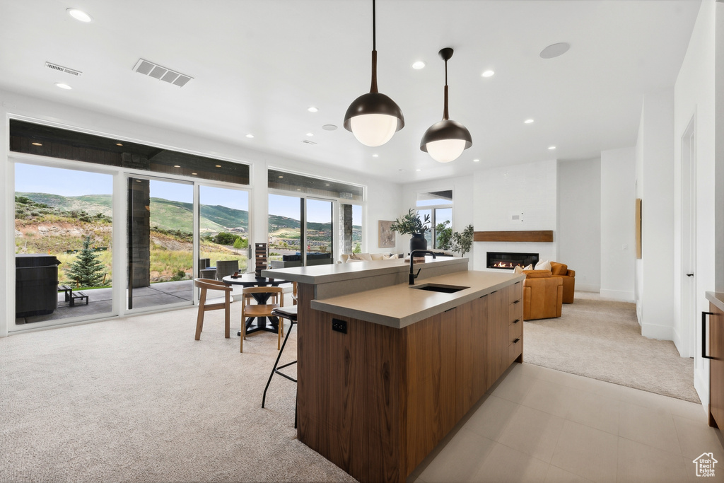 Kitchen with a breakfast bar, sink, pendant lighting, light colored carpet, and an island with sink