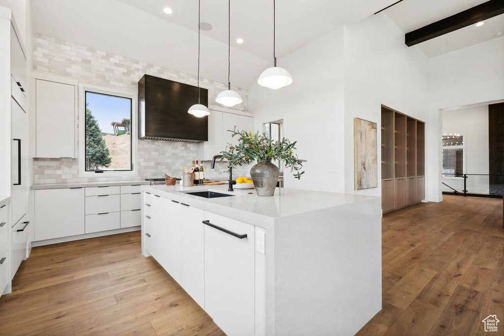 Kitchen featuring decorative light fixtures, white cabinetry, sink, light hardwood / wood-style floors, and backsplash