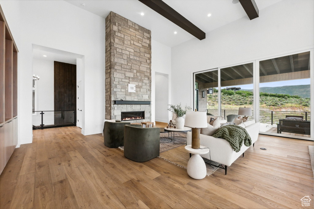 Living room featuring a stone fireplace, beam ceiling, hardwood / wood-style flooring, and a towering ceiling