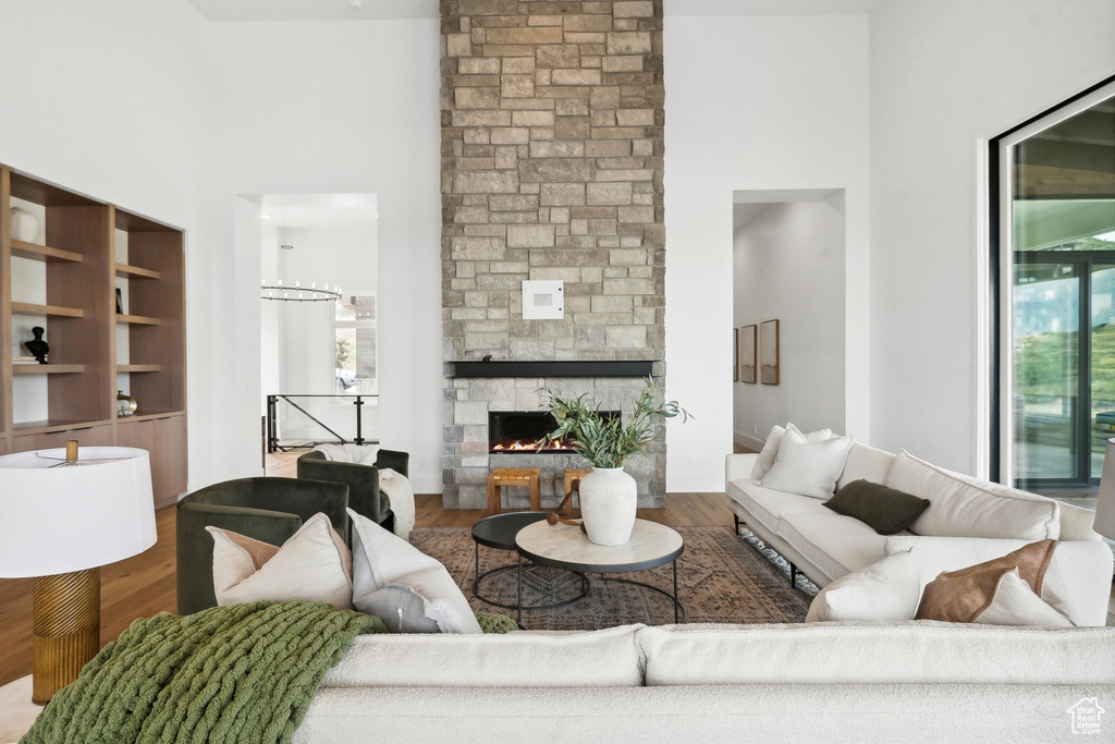 Living room featuring hardwood / wood-style flooring, built in shelves, a stone fireplace, and a towering ceiling