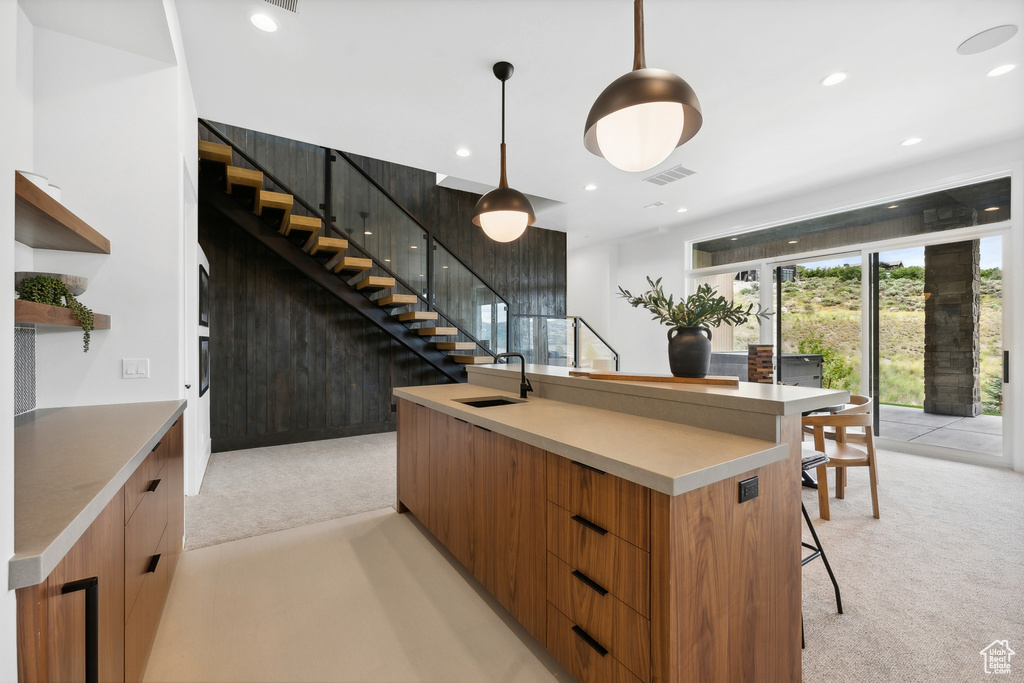 Kitchen featuring sink, pendant lighting, light colored carpet, and a center island with sink