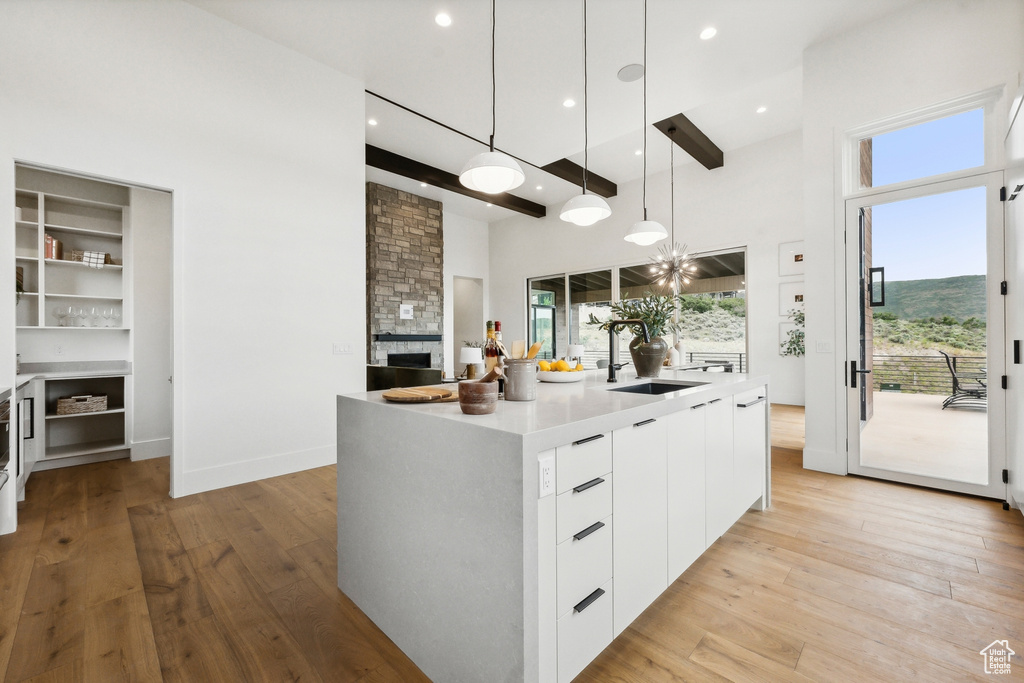 Kitchen featuring white cabinets, a fireplace, pendant lighting, light hardwood / wood-style floors, and a kitchen island with sink