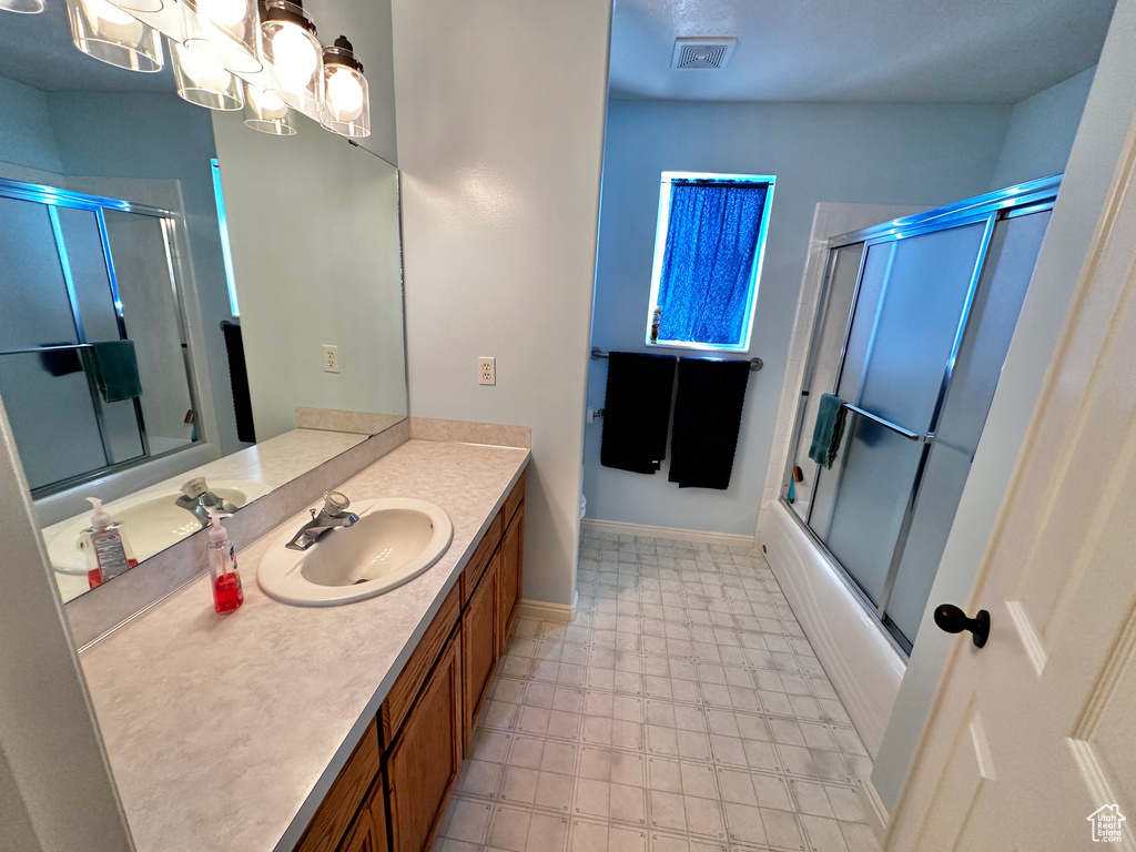 Bathroom with tile patterned flooring, a notable chandelier, shower / bath combination with glass door, and vanity