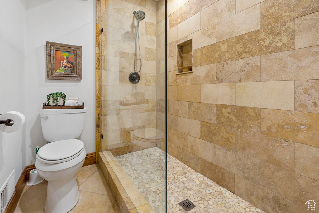 Bathroom with tile patterned flooring, toilet, and a tile shower