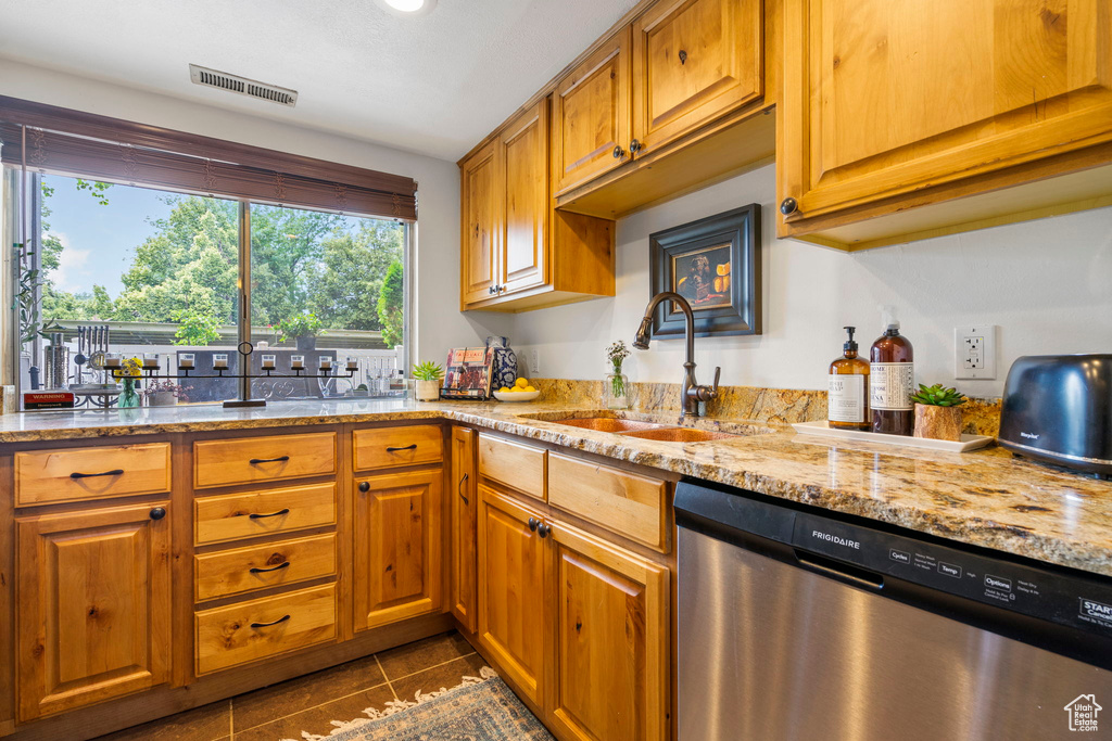 Kitchen featuring sink, dishwasher, light stone countertops, and dark tile patterned floors