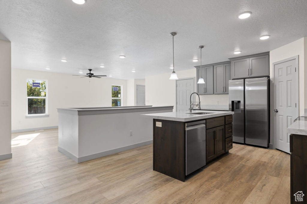 Kitchen with a kitchen island with sink, hanging light fixtures, sink, appliances with stainless steel finishes, and light hardwood / wood-style floors