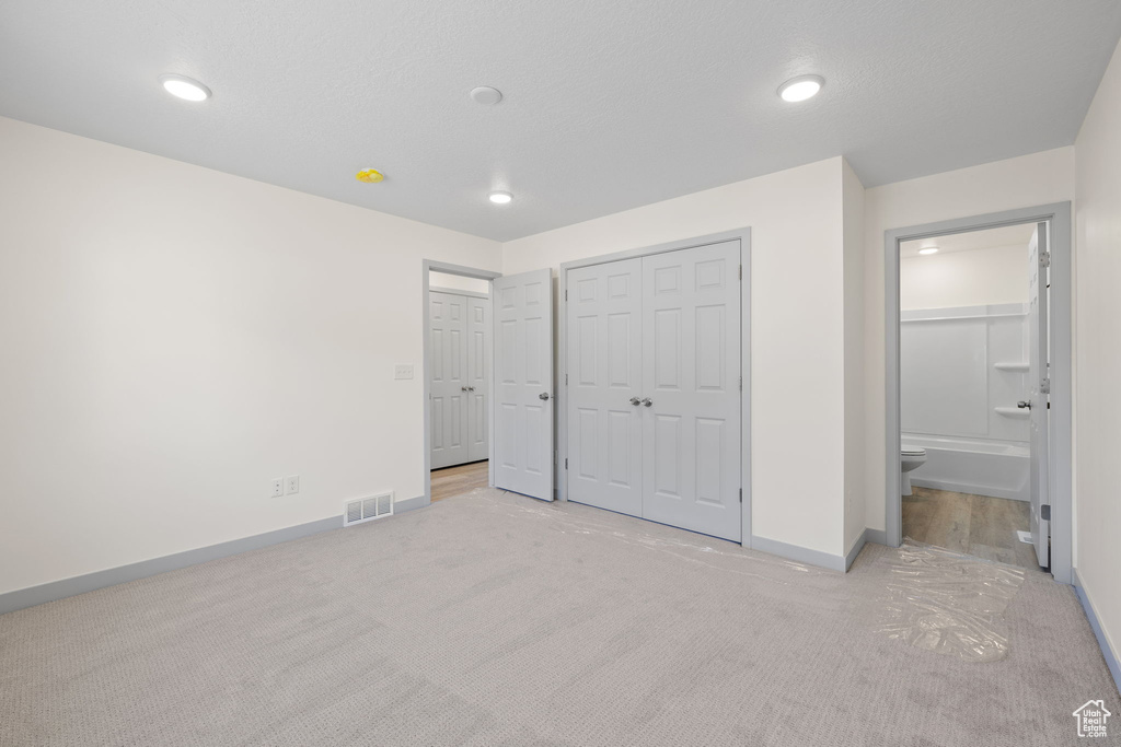 Unfurnished bedroom with a closet, ensuite bath, and light colored carpet