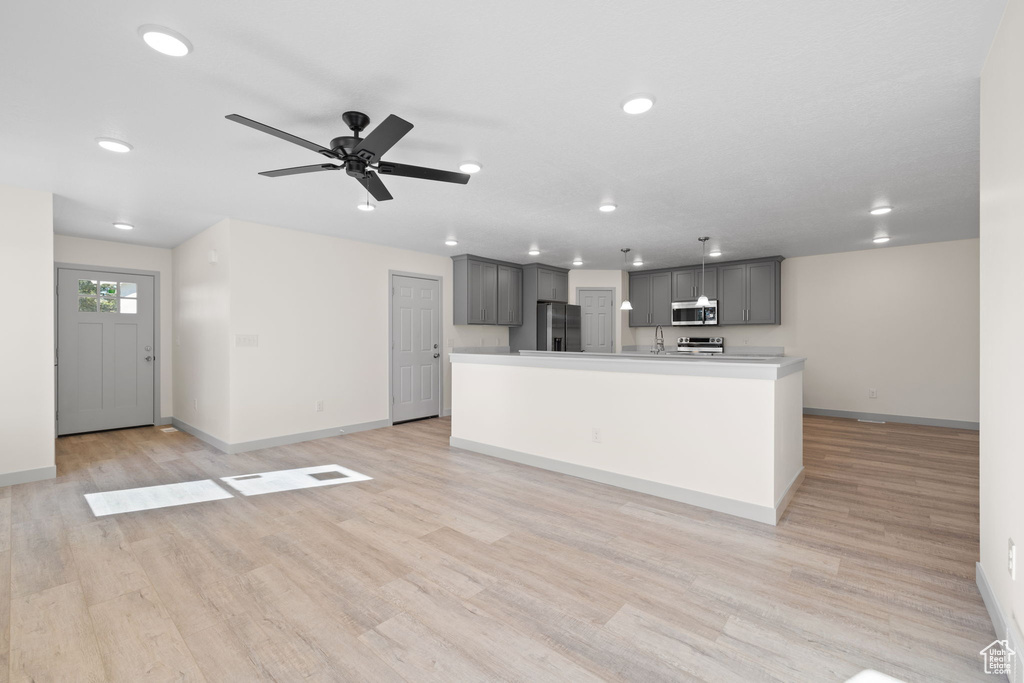 Kitchen with a center island with sink, ceiling fan, light wood-type flooring, gray cabinets, and stainless steel appliances