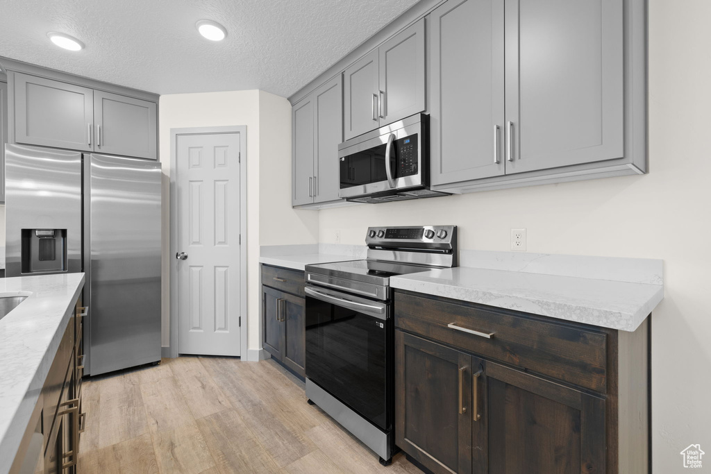 Kitchen featuring light stone counters, stainless steel appliances, a textured ceiling, and light hardwood / wood-style flooring