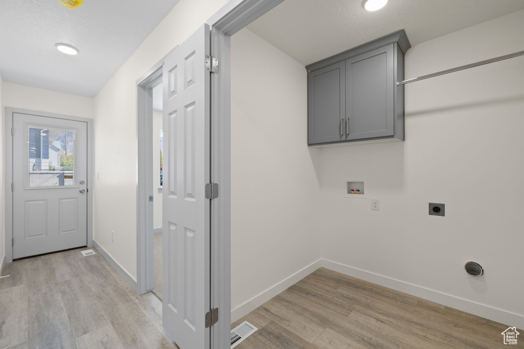 Laundry area with light wood-type flooring, a textured ceiling, electric dryer hookup, washer hookup, and cabinets