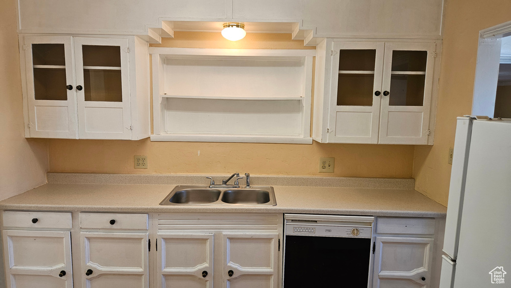 Kitchen with white fridge, sink, black dishwasher, and white cabinetry