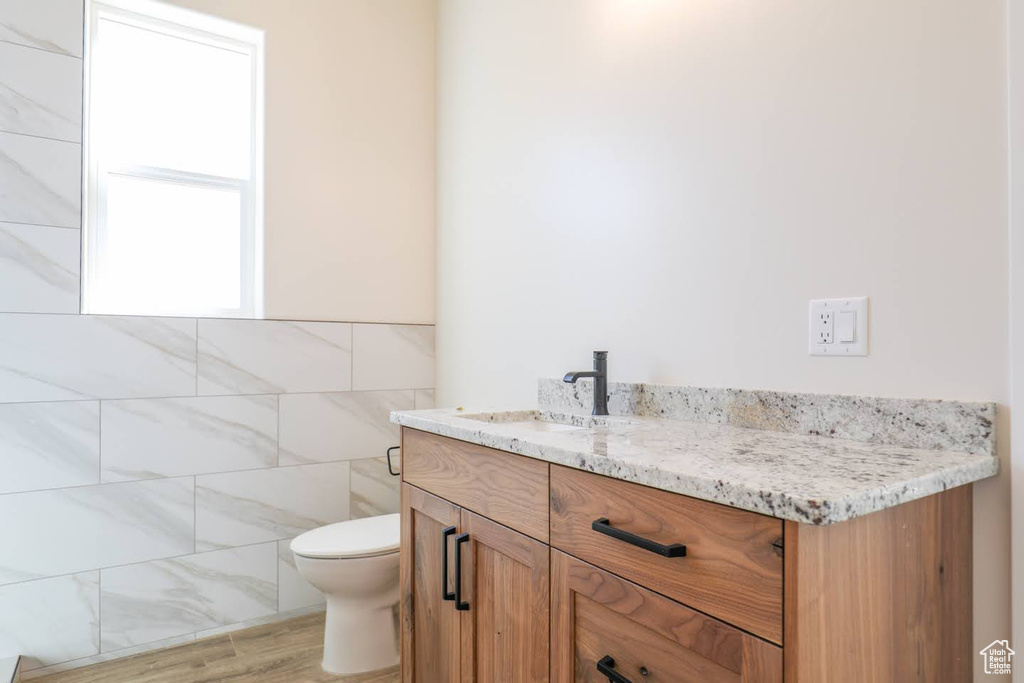 Bathroom featuring wood-type flooring, vanity, tile walls, and toilet