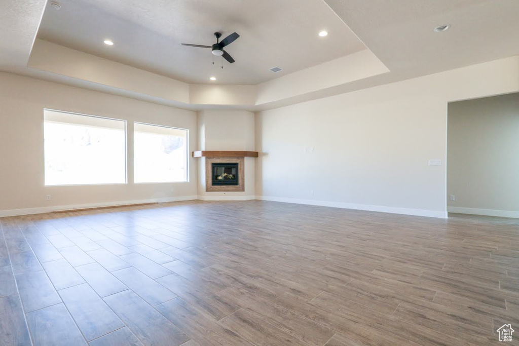 Unfurnished living room with ceiling fan, light wood-type flooring, and a raised ceiling