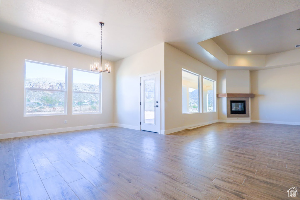 Unfurnished living room with hardwood / wood-style flooring, a notable chandelier, a textured ceiling, and a healthy amount of sunlight