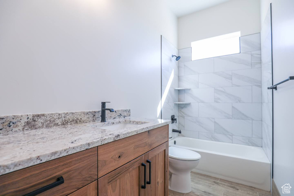 Full bathroom featuring wood-type flooring, tiled shower / bath combo, vanity, and toilet