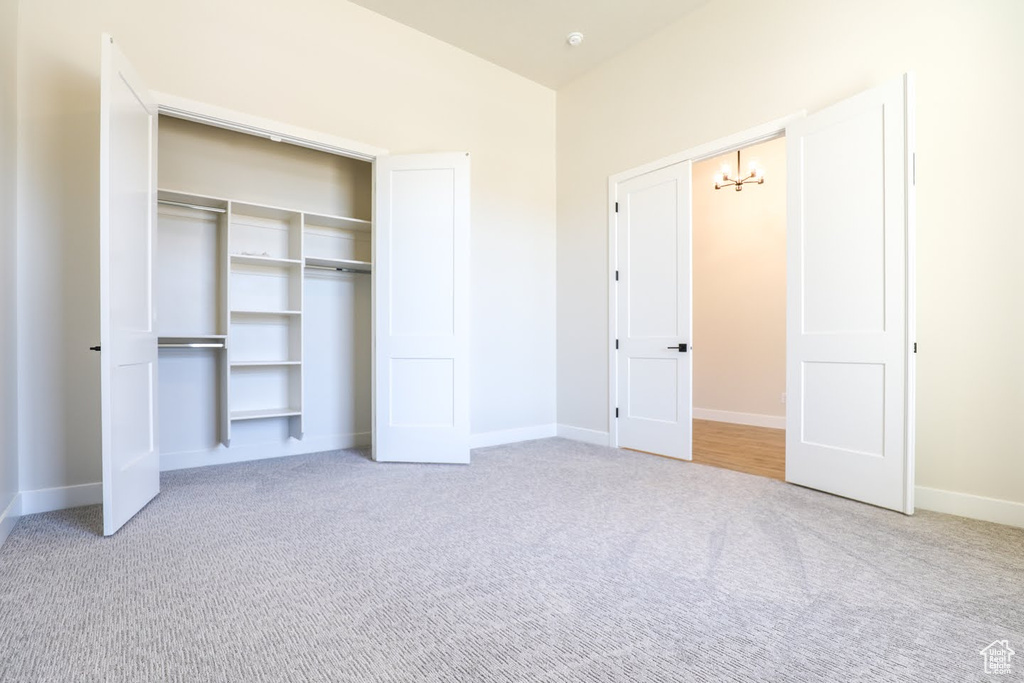 Unfurnished bedroom featuring light carpet, a closet, and an inviting chandelier