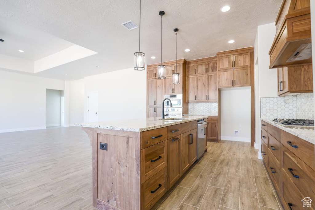 Kitchen with premium range hood, an island with sink, decorative light fixtures, and light hardwood / wood-style floors