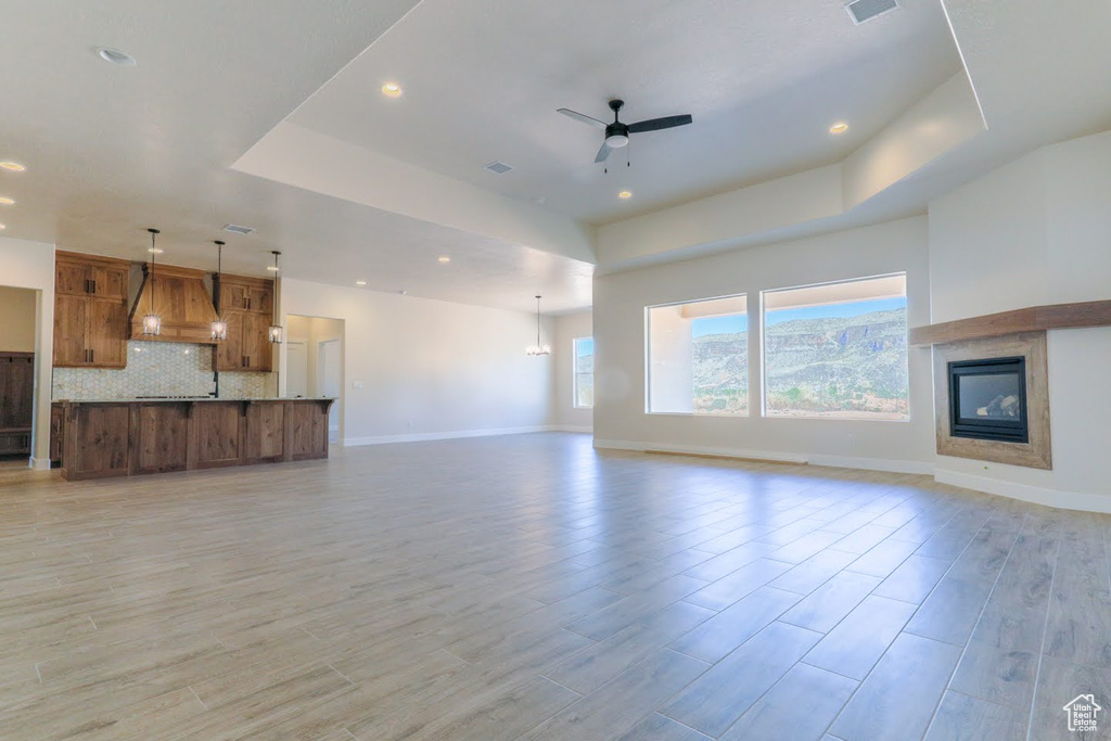 Unfurnished living room featuring light wood-type flooring, a tray ceiling, and ceiling fan