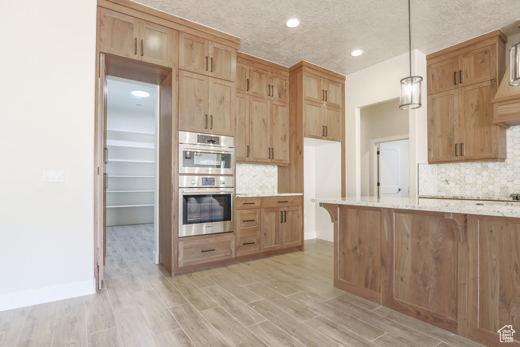 Kitchen with light hardwood / wood-style floors, a textured ceiling, tasteful backsplash, hanging light fixtures, and light stone countertops