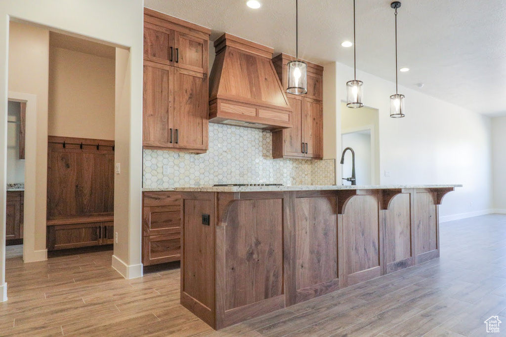 Kitchen featuring custom range hood, hanging light fixtures, light hardwood / wood-style flooring, and stovetop