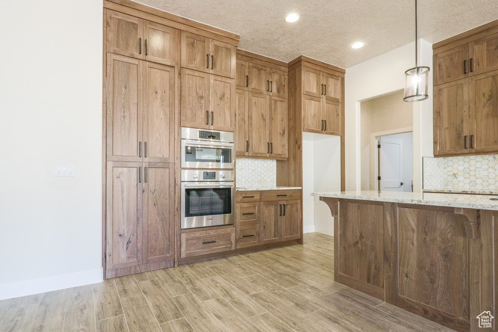 Kitchen with light stone countertops, light hardwood / wood-style floors, tasteful backsplash, and stainless steel double oven