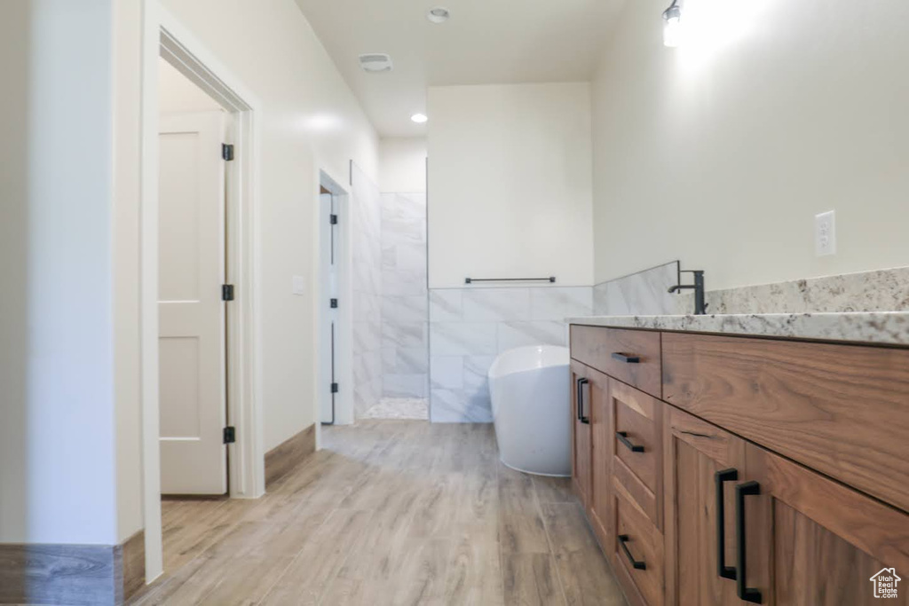 Bathroom with independent shower and bath, hardwood / wood-style flooring, vanity, and tile walls