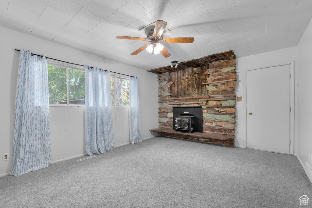 Unfurnished living room with carpet floors, a fireplace, ceiling fan, and a wood stove