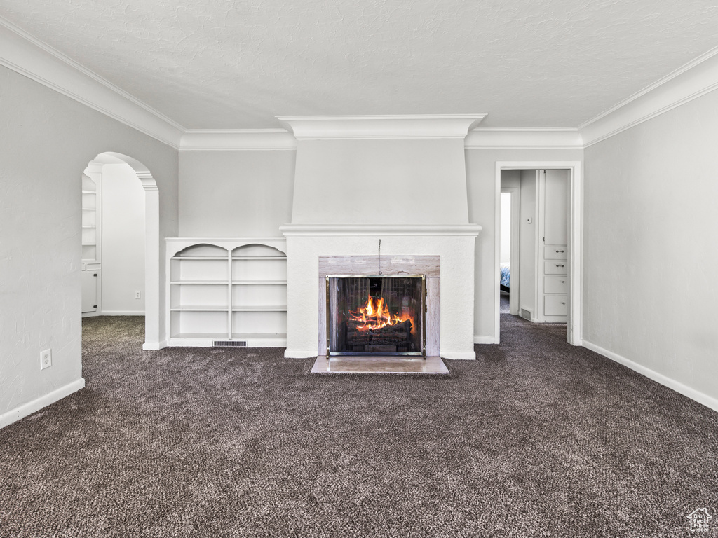 Unfurnished living room with crown molding, a tile fireplace, and dark colored carpet