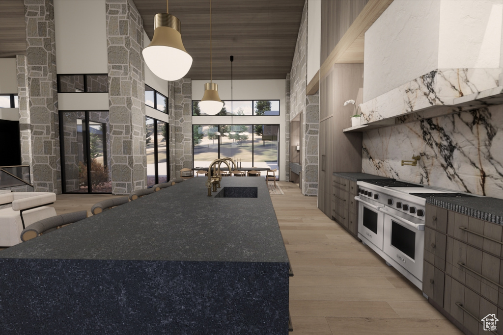 Kitchen featuring range with two ovens, hanging light fixtures, sink, light hardwood / wood-style flooring, and a towering ceiling