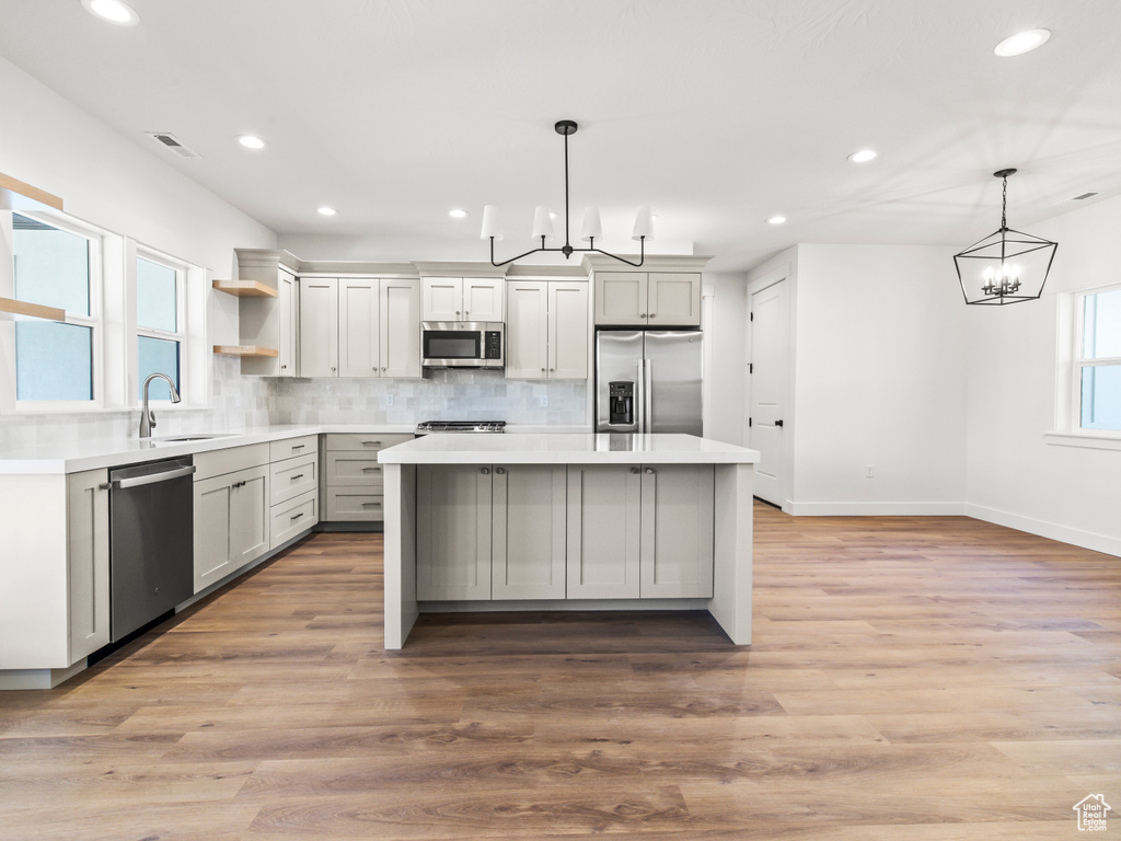 Kitchen with appliances with stainless steel finishes, a kitchen island, decorative backsplash, light wood-type flooring, and a chandelier