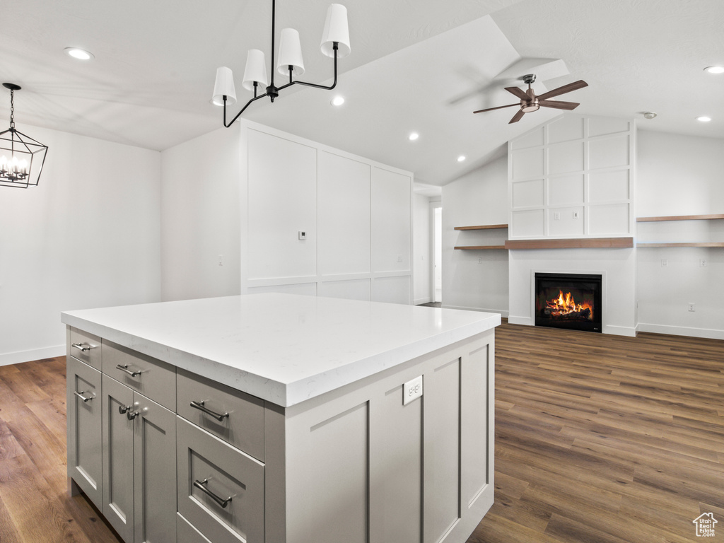 Kitchen featuring ceiling fan with notable chandelier, a center island, dark hardwood / wood-style flooring, hanging light fixtures, and a fireplace