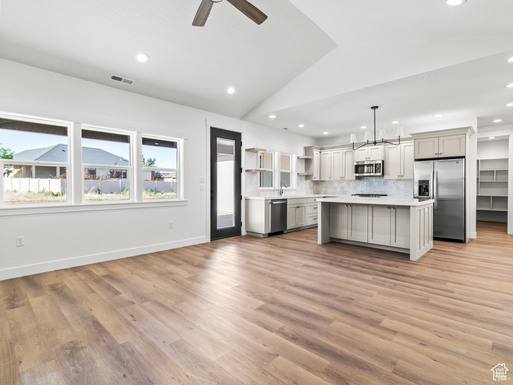 Kitchen with light hardwood / wood-style floors, pendant lighting, a kitchen island, and stainless steel appliances