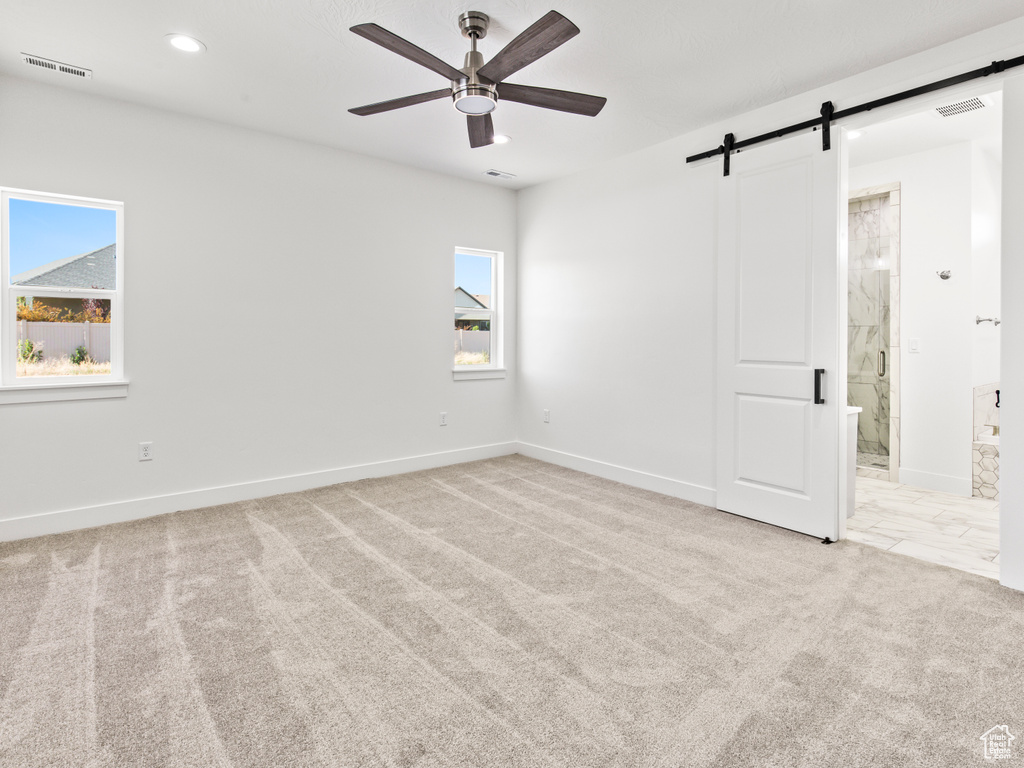 Unfurnished room featuring light carpet, ceiling fan, and a barn door