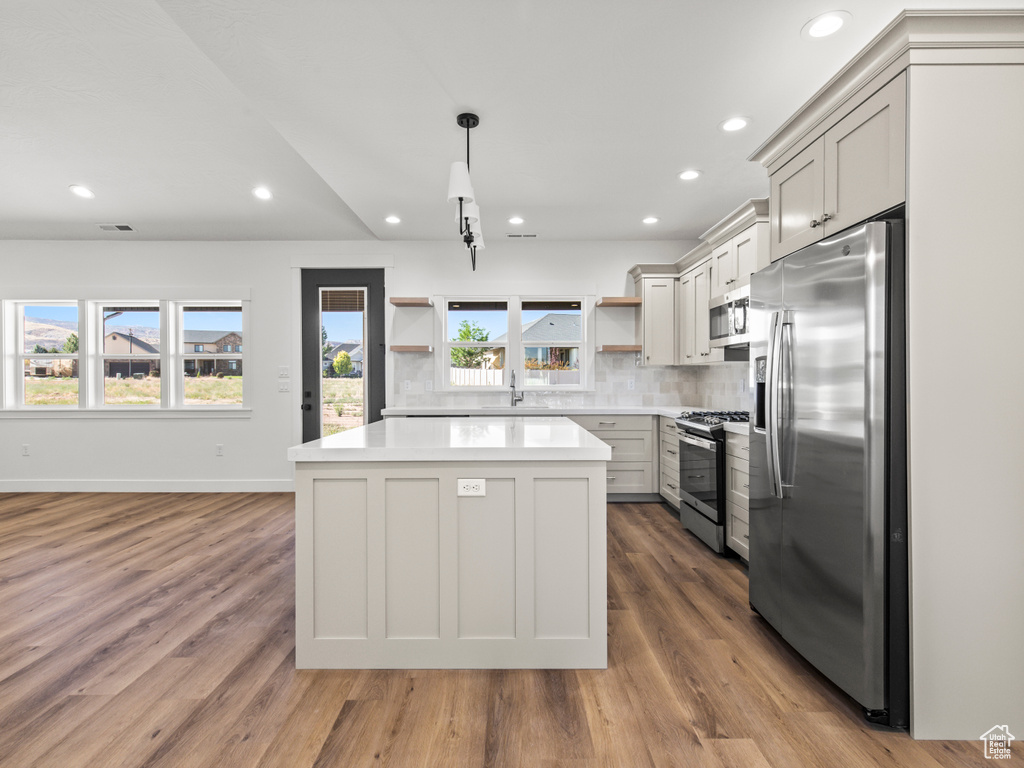 Kitchen featuring appliances with stainless steel finishes, decorative backsplash, hardwood / wood-style floors, and a kitchen island