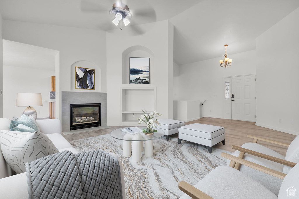 Living room with ceiling fan with notable chandelier, built in shelves, light hardwood / wood-style floors, a fireplace, and vaulted ceiling