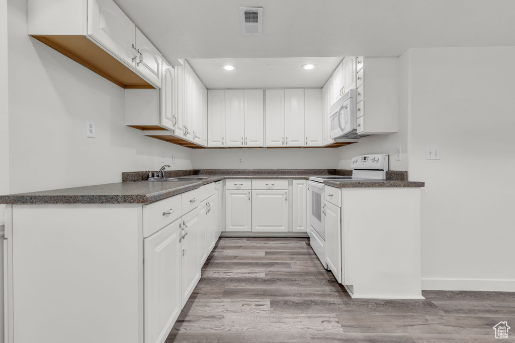 Kitchen with sink, white cabinetry, hardwood / wood-style flooring, and white appliances