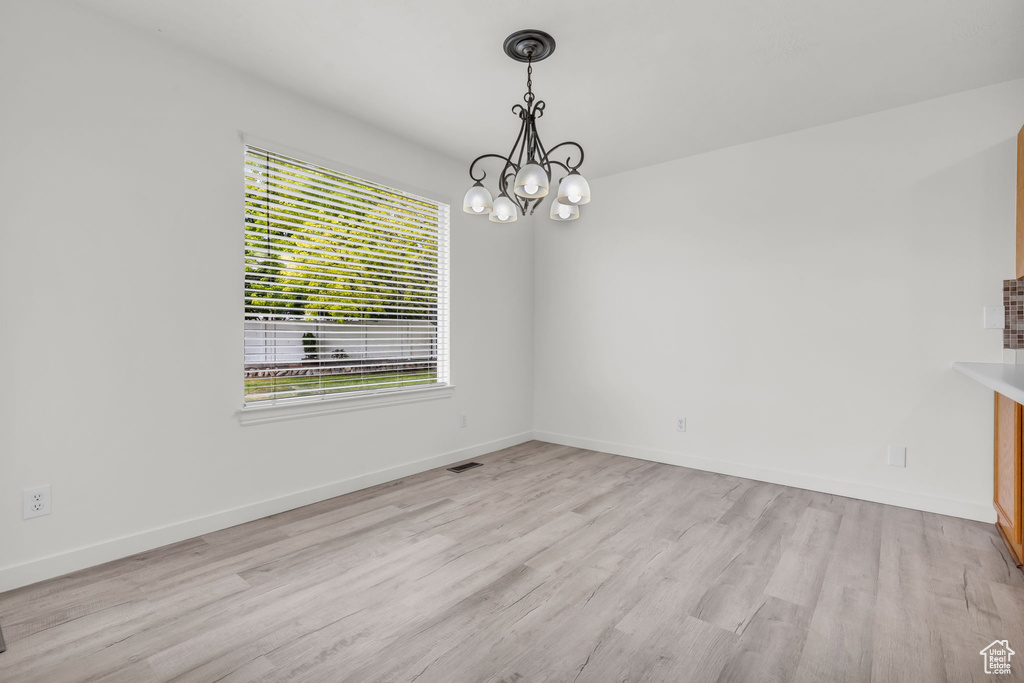 Unfurnished room featuring a chandelier and light hardwood / wood-style flooring